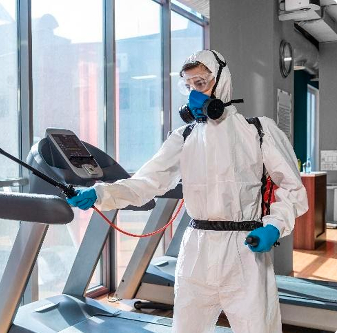 Commercial cleaner in white coveralls wiping the arm of a treadmill at a Kansas fitness center.
