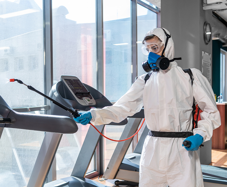 Commercial cleaner in white coveralls wiping the arm of a treadmill at a Kansas City fitness center.