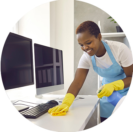 Smiling female cleaner using commercial cleaning products to properly disinfect a computer monitor in an office environment.